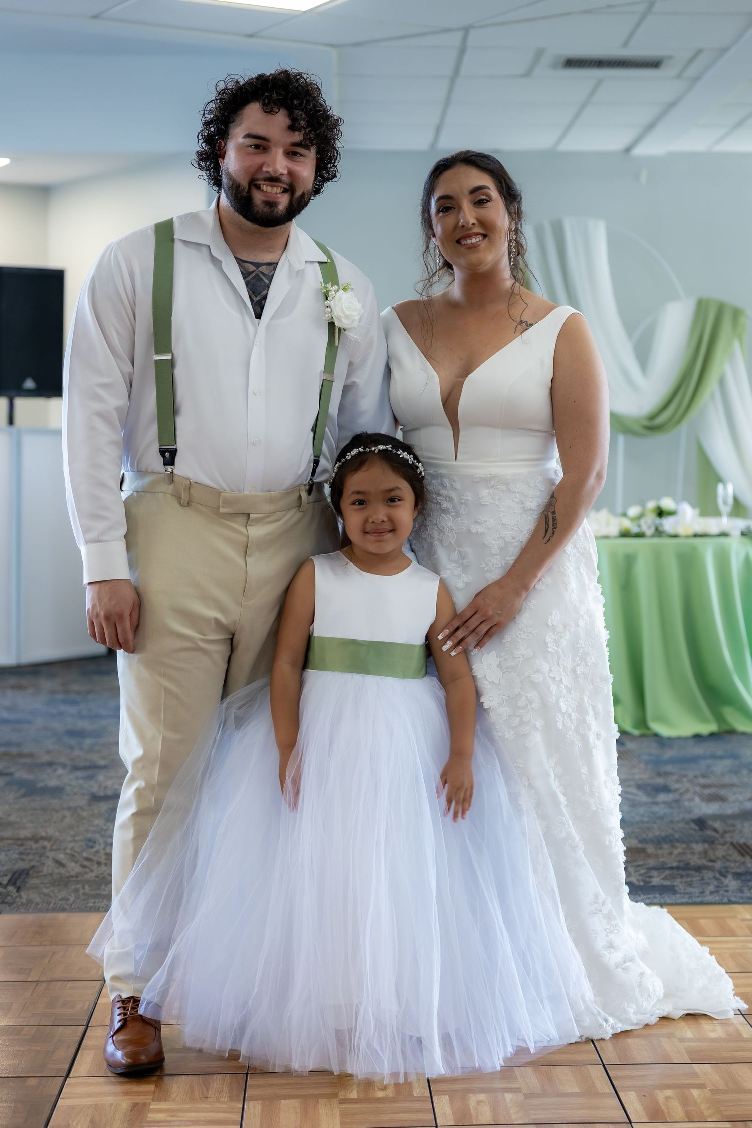 Wedding party members in white outfits pose together on a marbled floor with green accents.