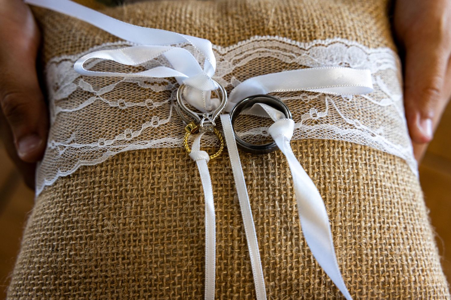 A rustic burlap ring bearer pillow decorated with white lace ribbons.
