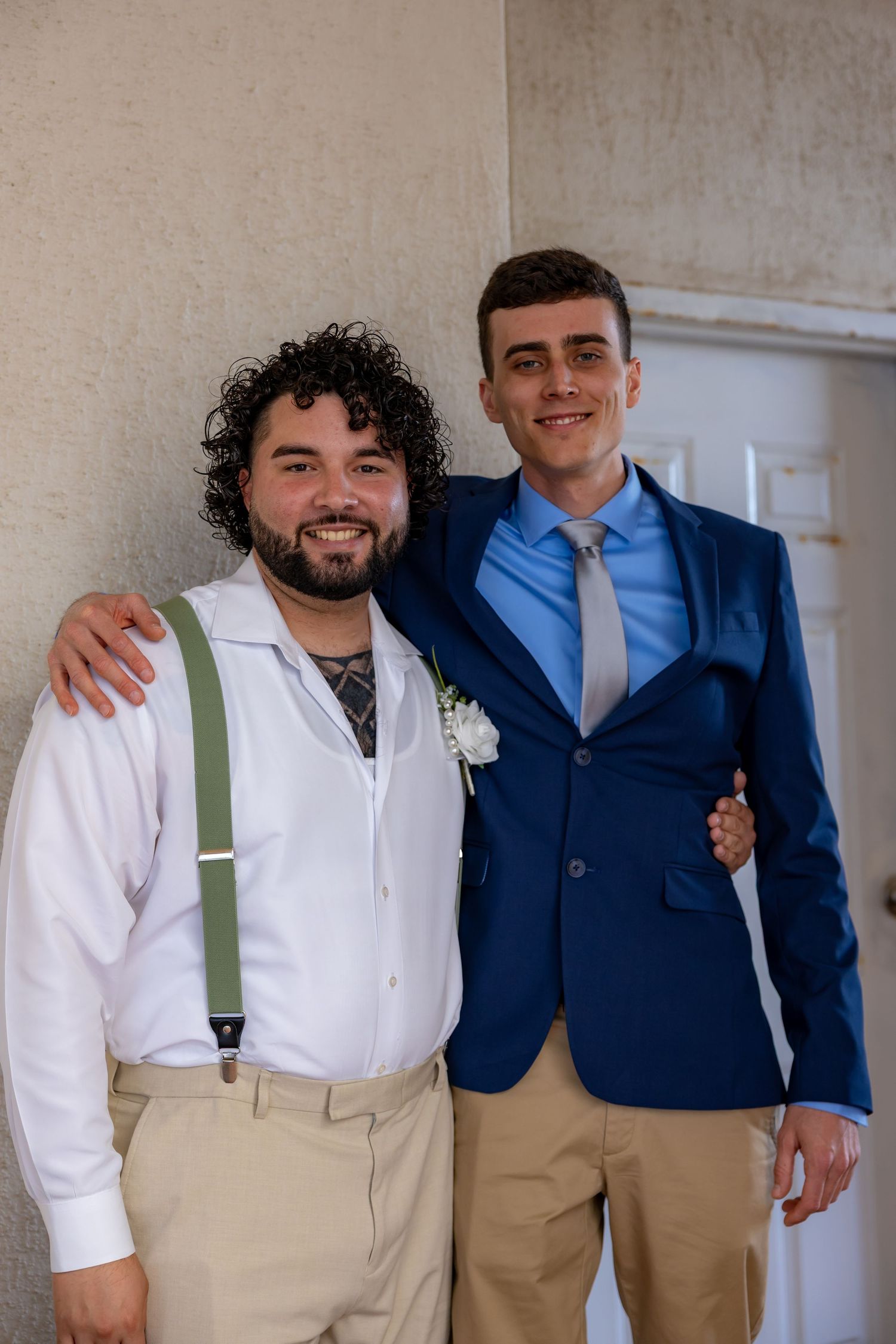 Groomsmen in white shirts and khaki pants with suspenders pose together indoors.