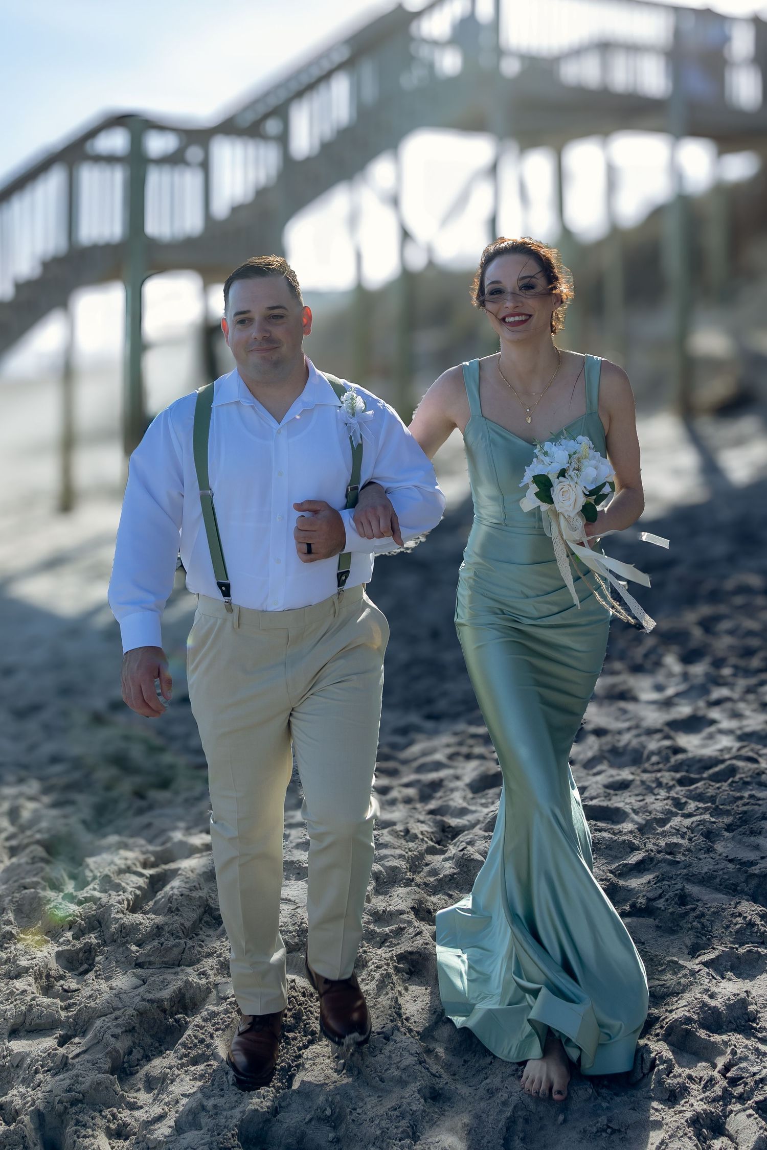 Wedding party members pose on beach sand in light colored formal attire.