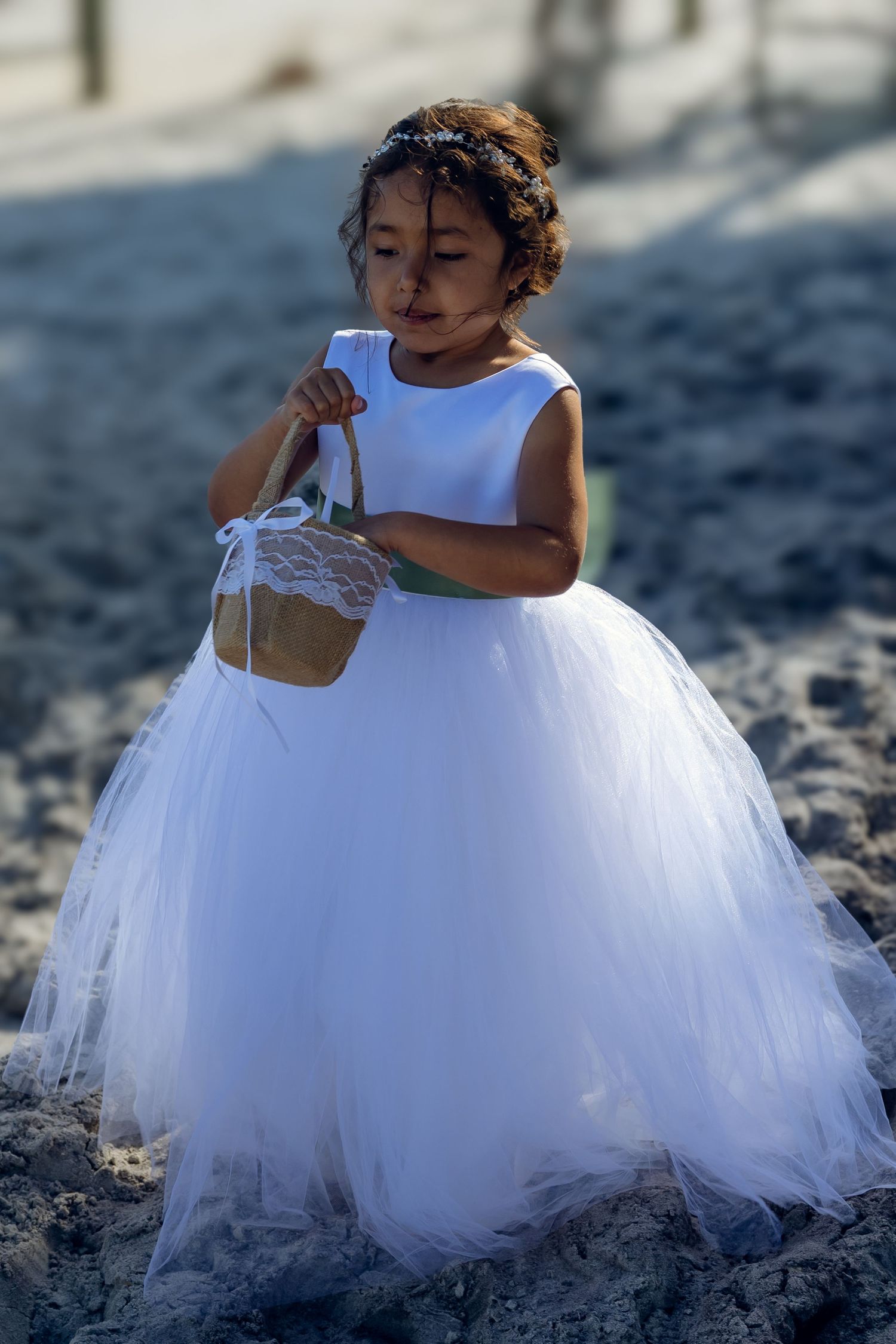 Child in flowing white tulle dress plays in beach sand during wedding.