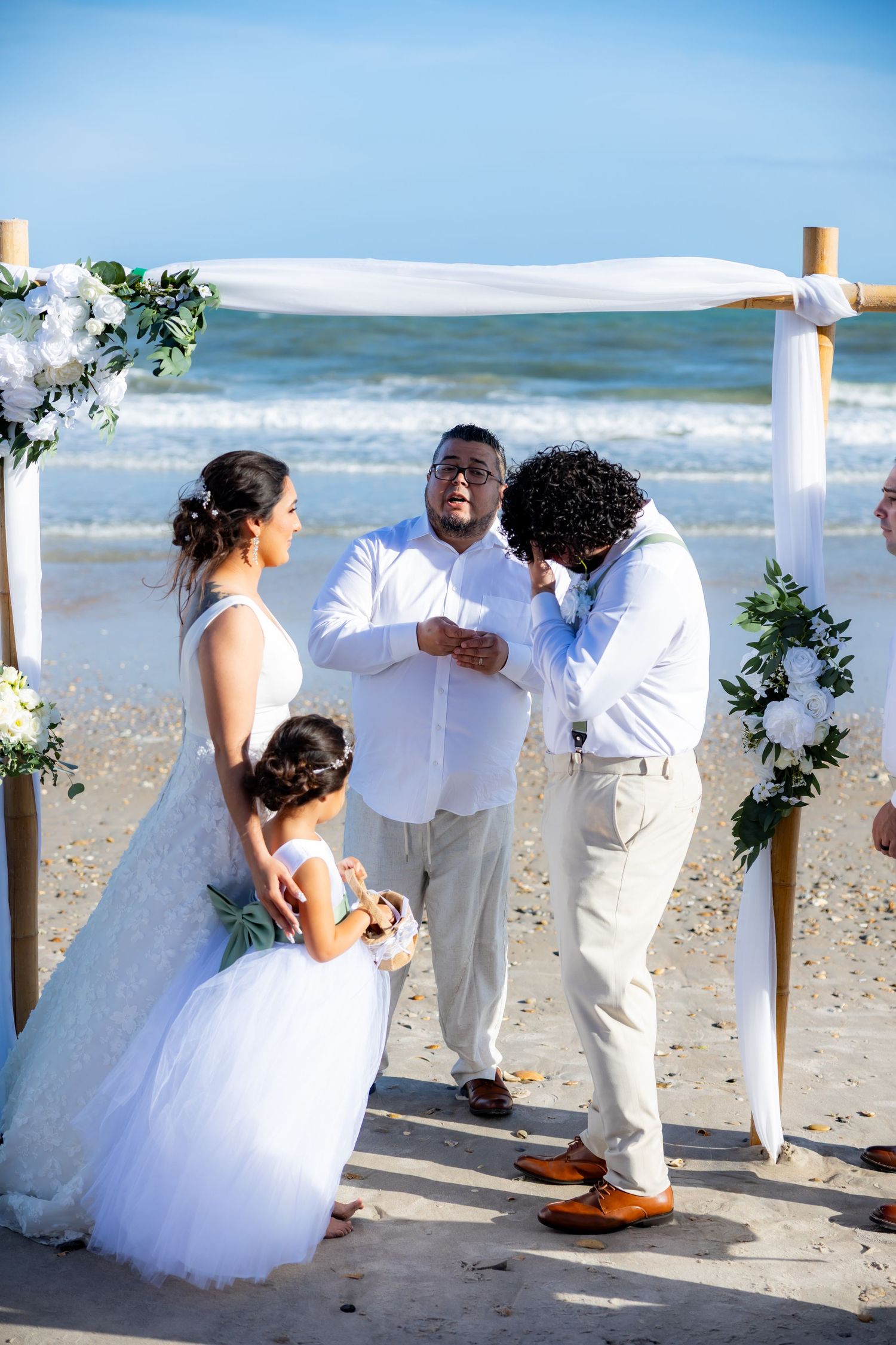 A joyful moment during a beachside wedding ceremony with attendants laughing under a decorated white arch.