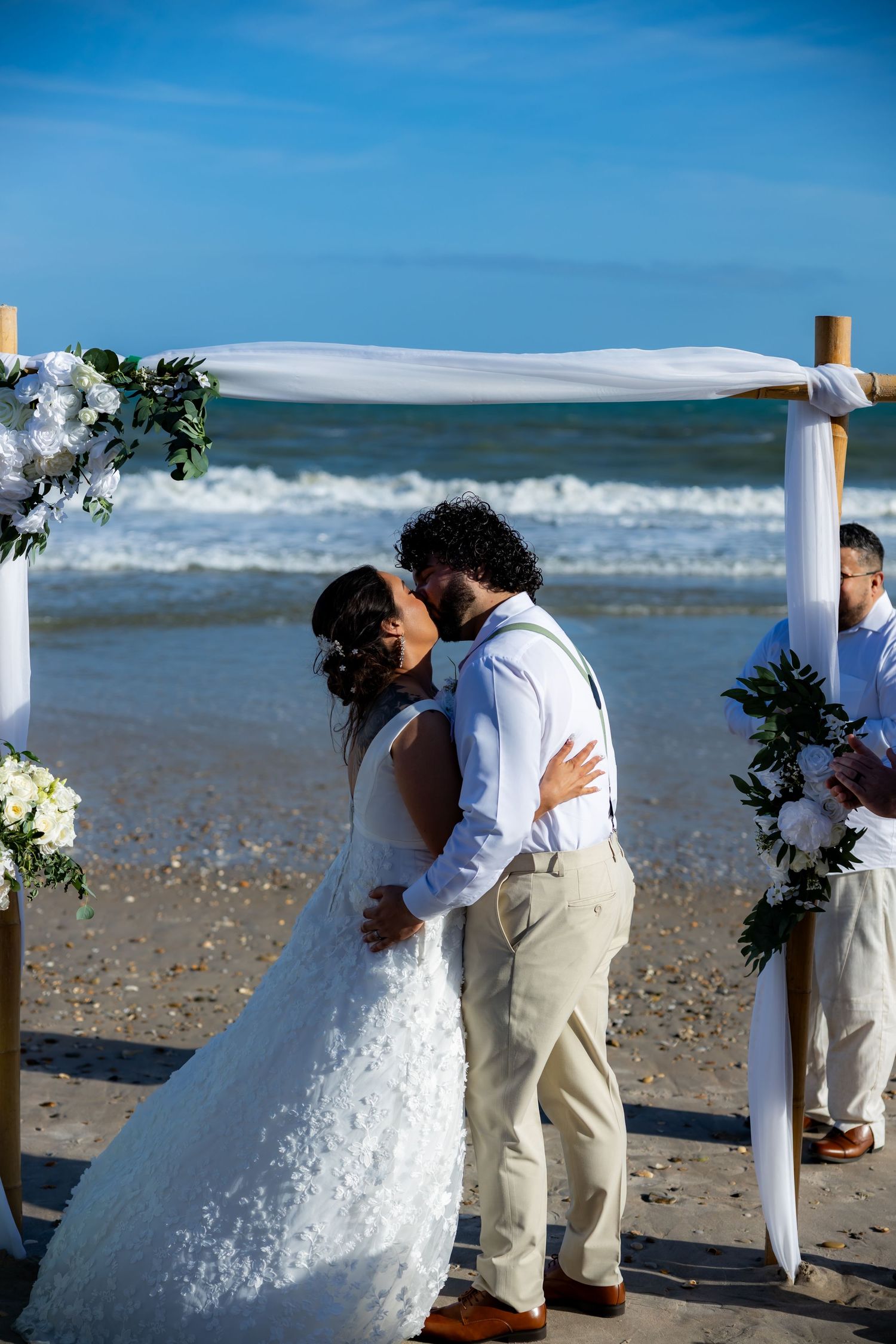 A beachside wedding ceremony with white decorative posts and crashing waves in the background.