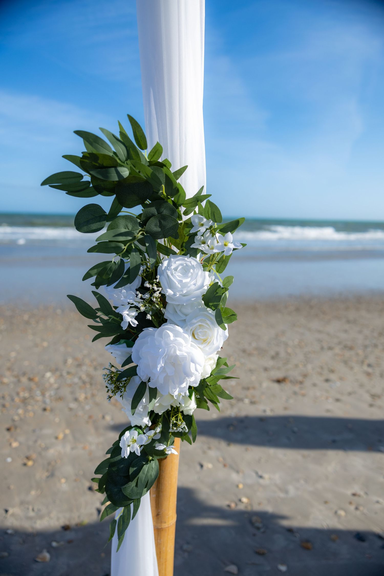 A series of four connected photos showing a beach wedding arch decorated with white flowers and greenery against ocean waves.