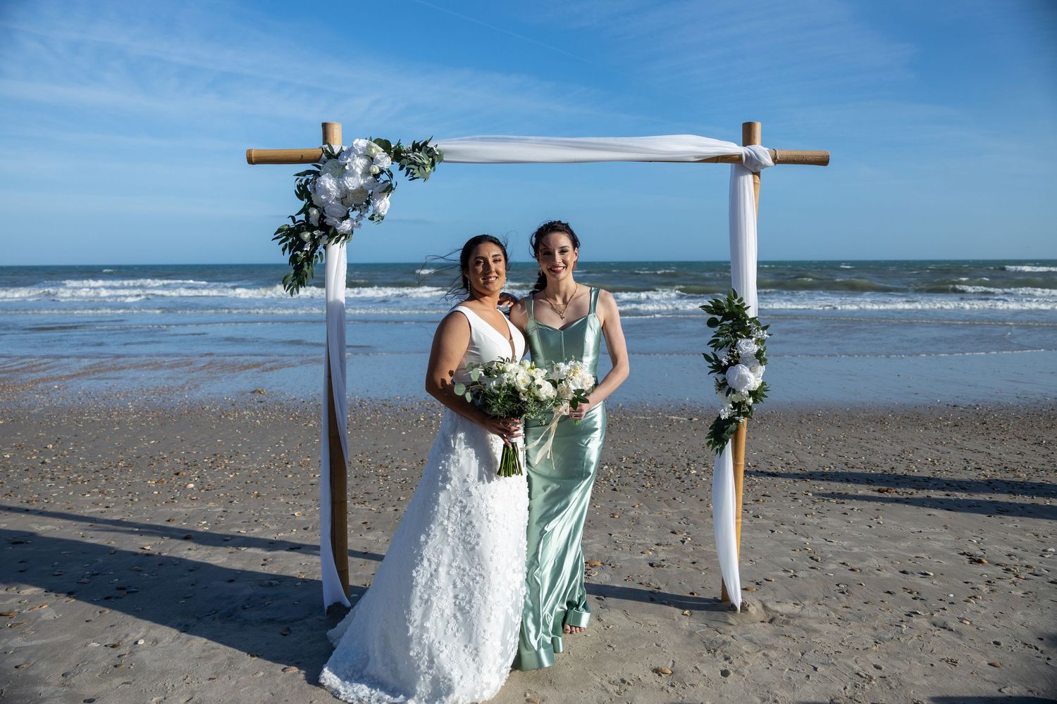 Beach wedding ceremony setup featuring a wooden arch decorated with florals against the ocean backdrop.