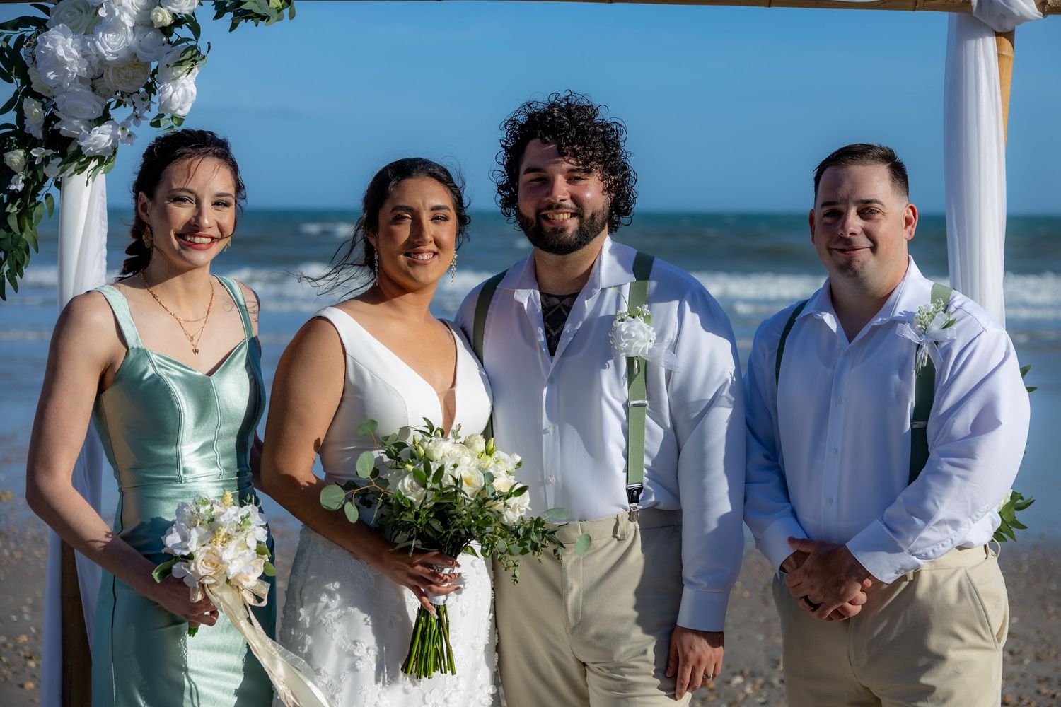 Wedding party in coordinated beachwear poses together on sandy shore.