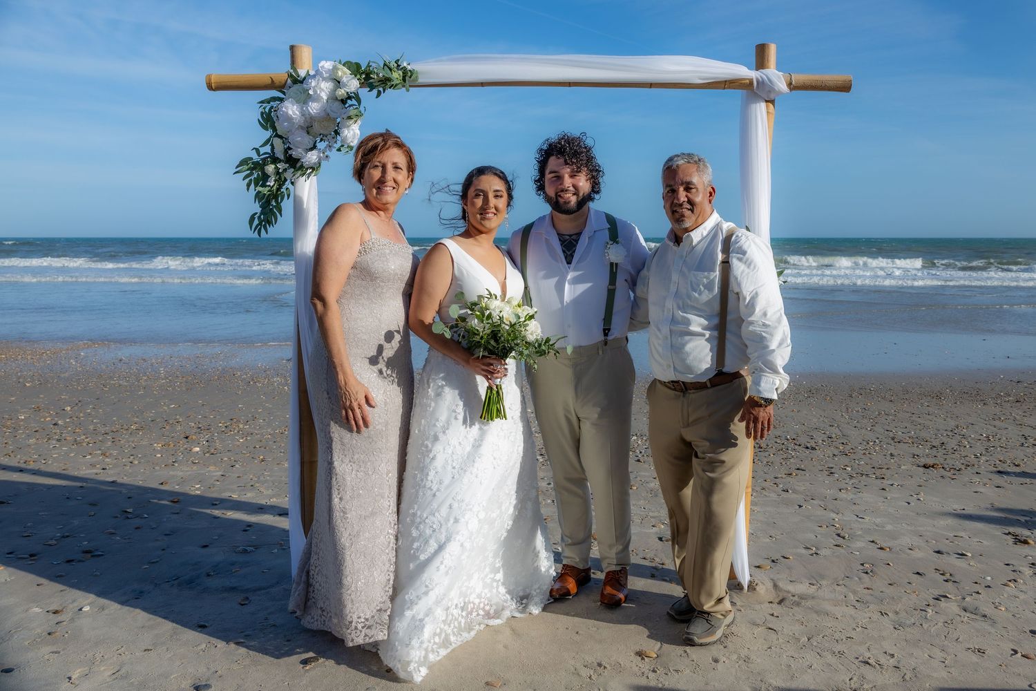 A beach wedding ceremony setup with wooden arch and floral decorations against ocean backdrop.