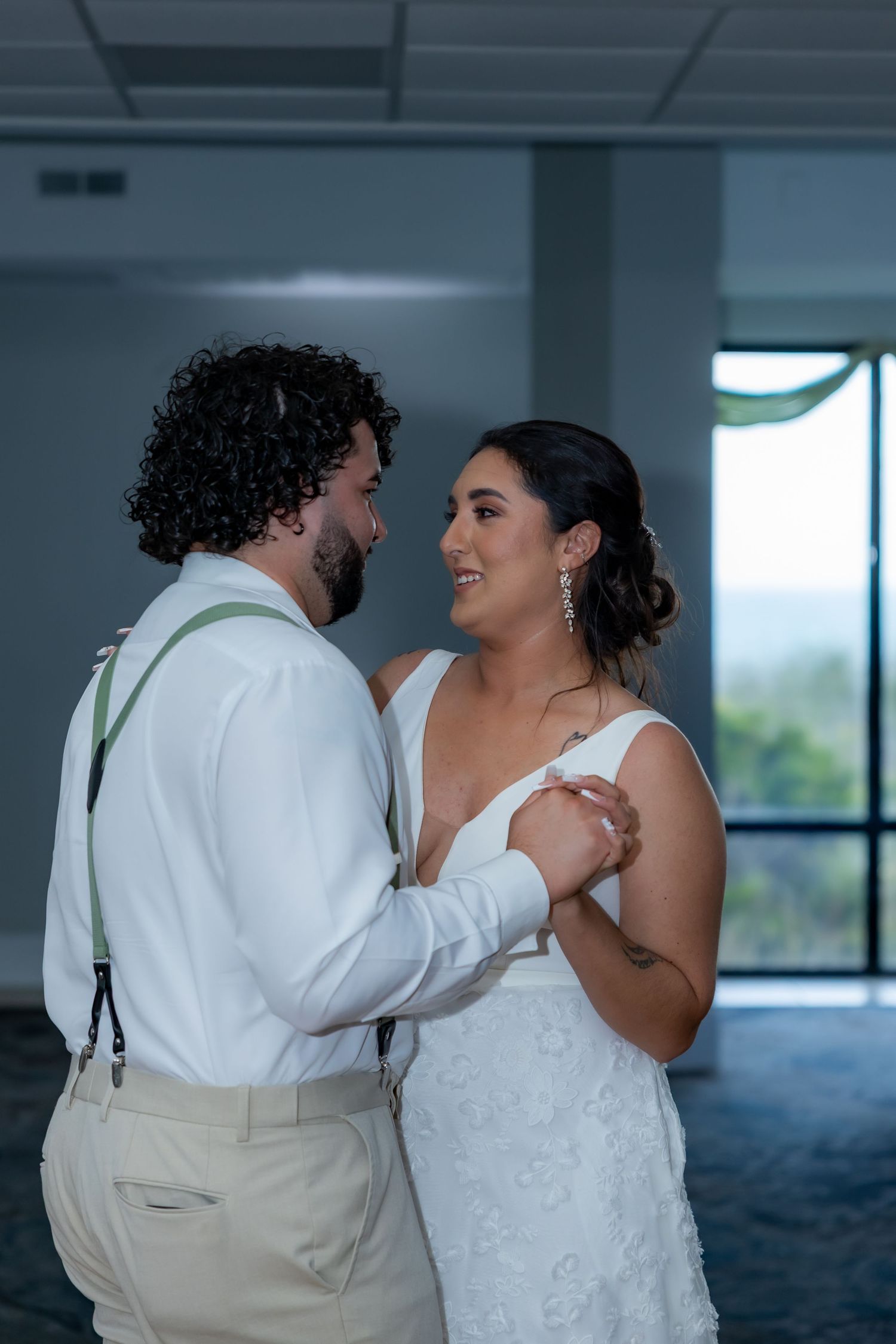 A couple sharing an intimate moment in white wedding attire during their celebration in a modern indoor setting.