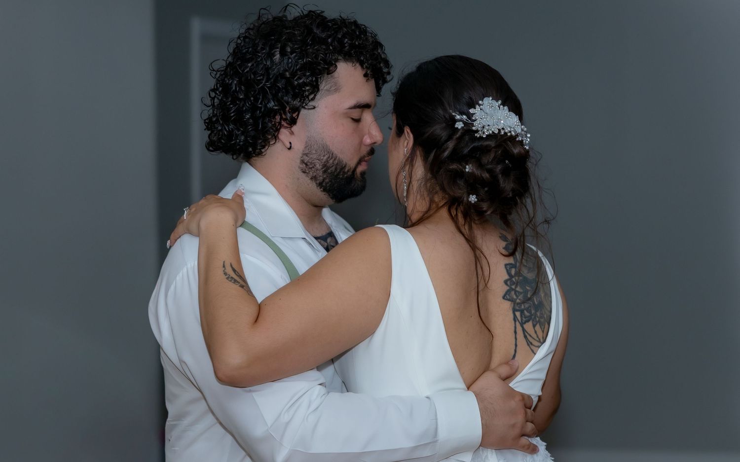 A romantic couple embraces in an intimate moment against a gray background during their wedding celebration.