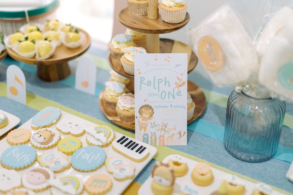 Delicate pastel blue and cream colored cookies and cupcakes arranged on a dessert table with decorative elements.