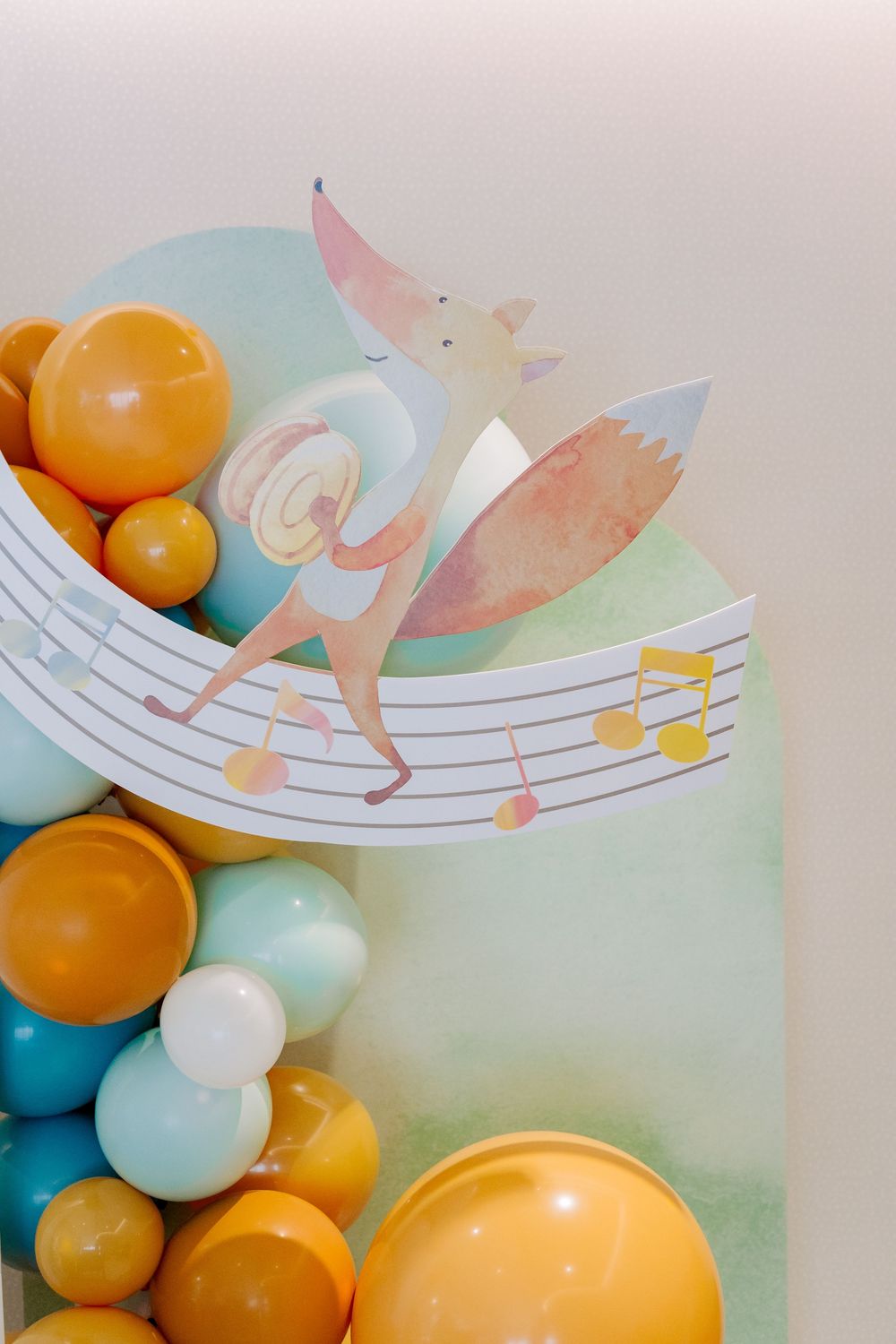 Decorative music notes with orange and blue balloons create a whimsical party backdrop with fairy illustration.