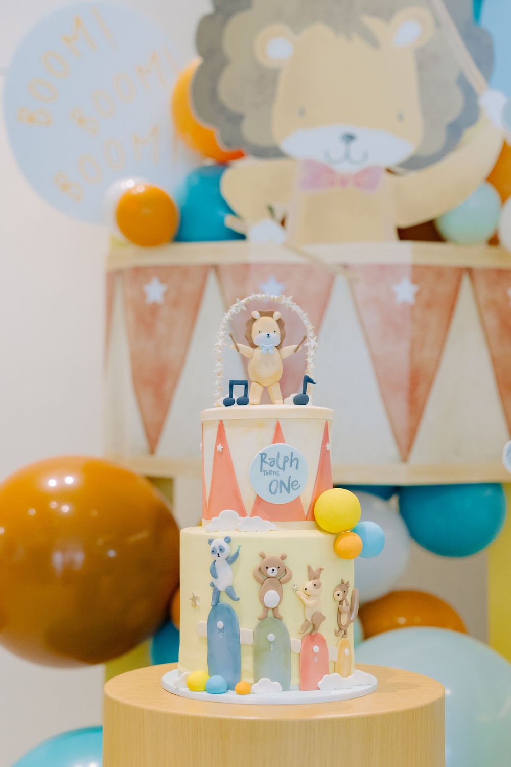 A festive baby shower cake decorated with pastel colors, bunnies, and musical notes stands on a wooden display stand.