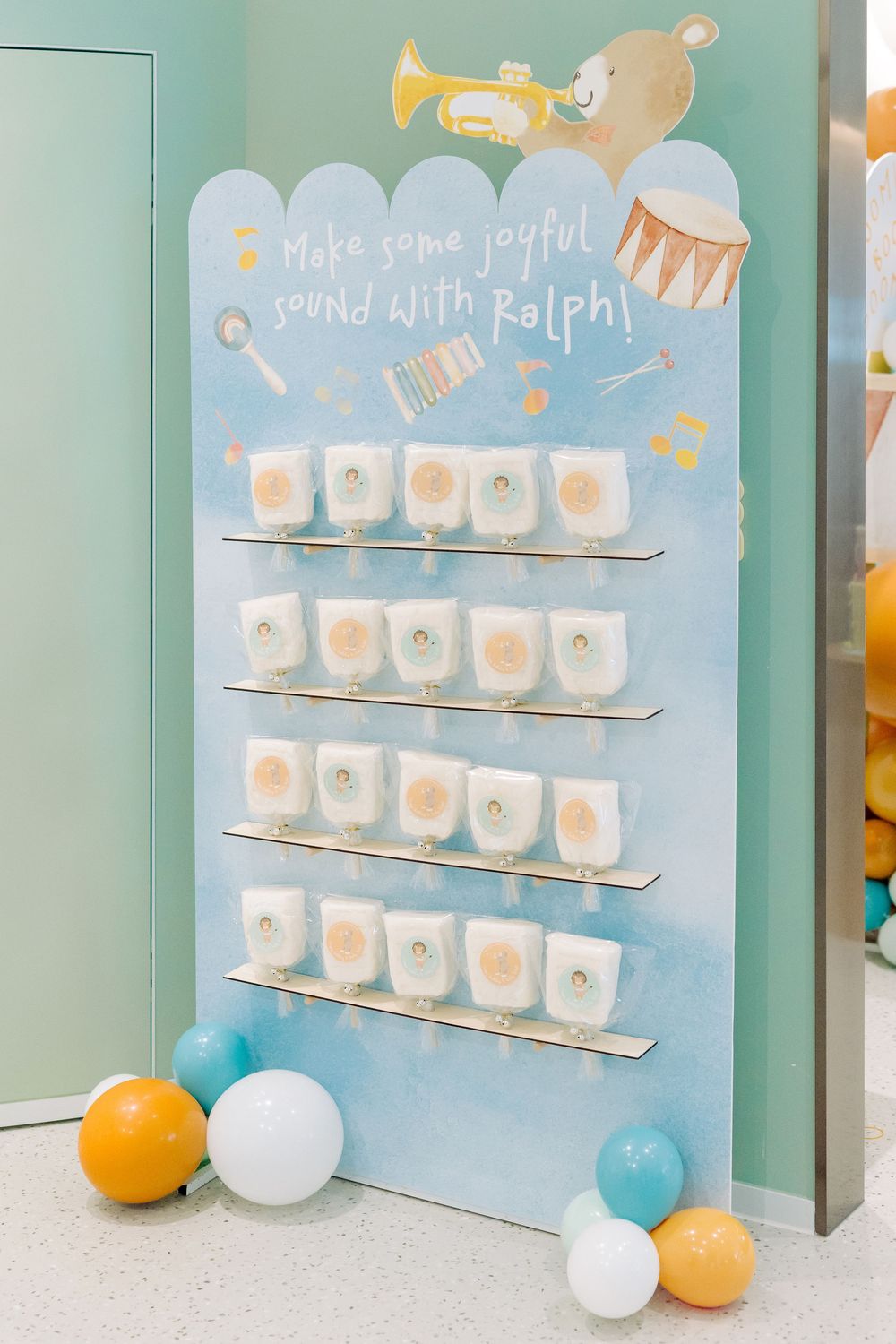 Soft green display board with small white shelves holding party cups and decorative balloons at the base.