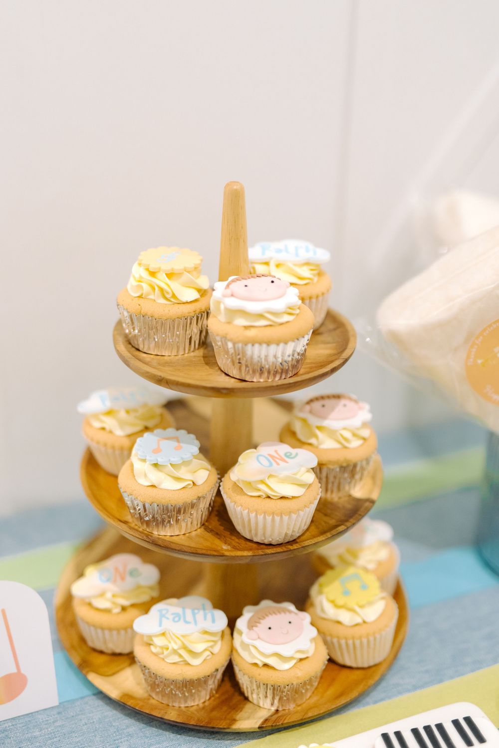 Gold tiered dessert stand displays delicate cupcakes decorated with soft blue and pink frosting details at a party.