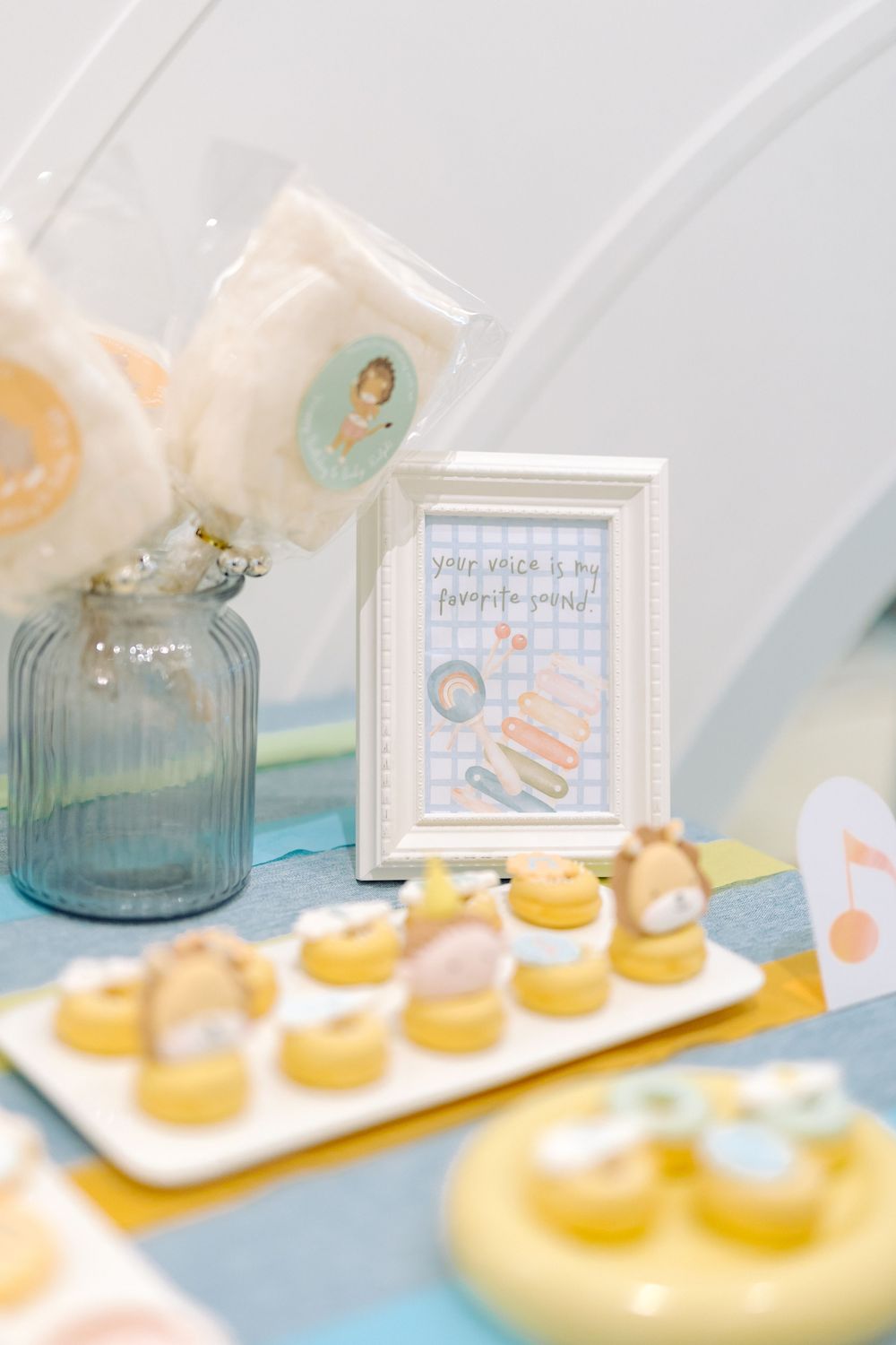 Small yellow glazed pastries arranged on a white serving platter with teal glass decor and framed artwork in background.