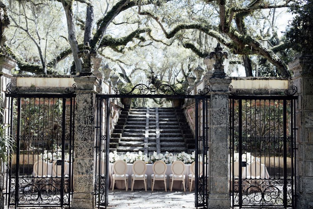 A rustic iron gate entrance leads to a tree-lined snowy path during winter.