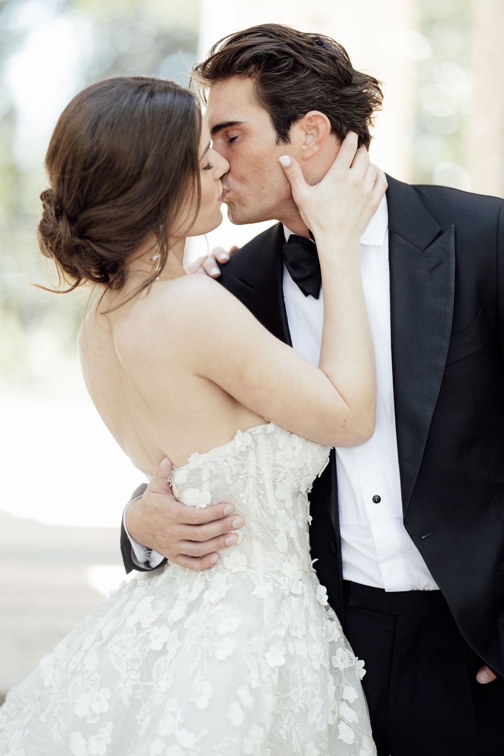 A romantic wedding moment as newlyweds share a kiss, bride in strapless floral gown and groom in classic tuxedo.