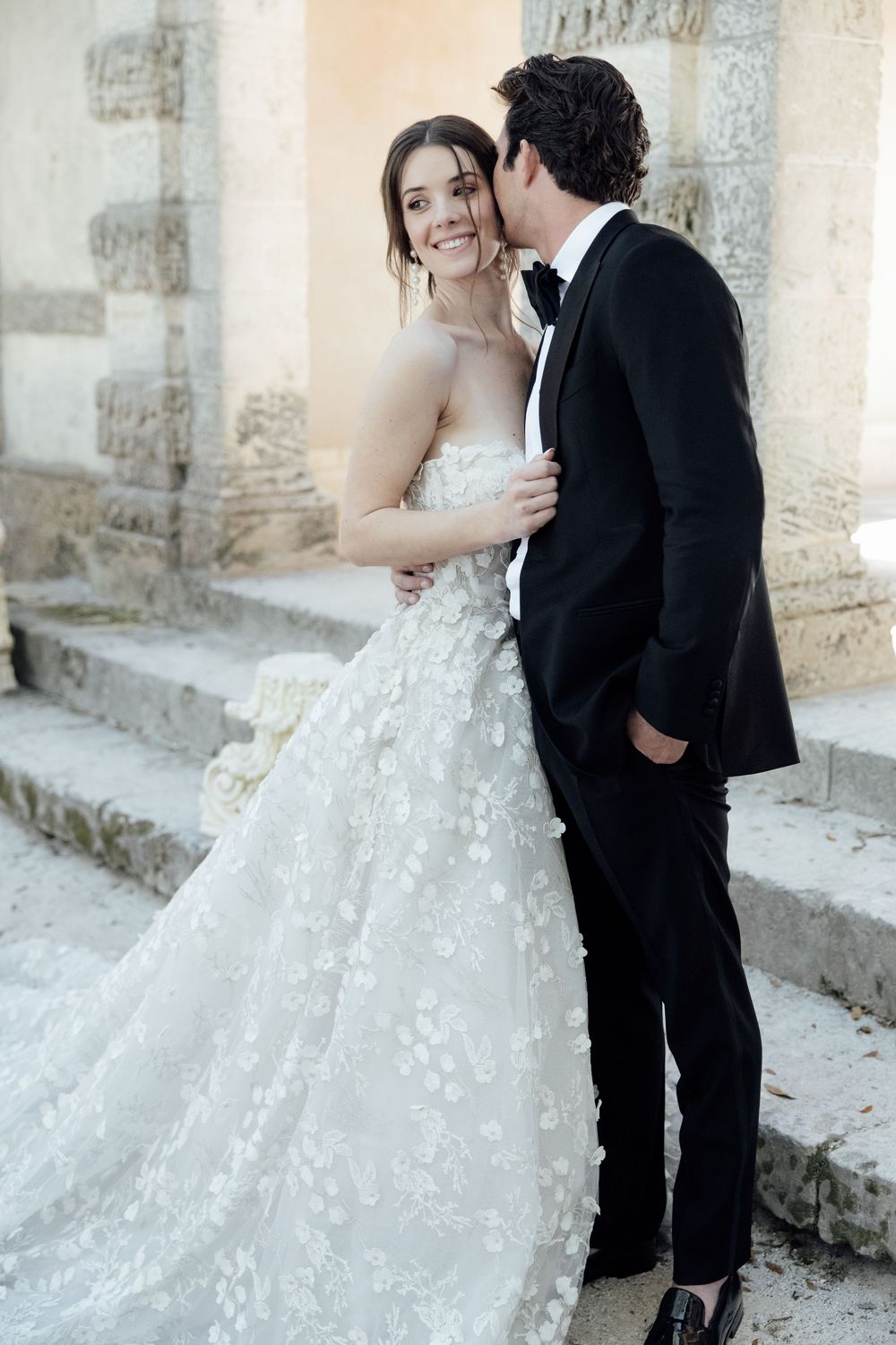 Wedding couple shares intimate moment on stone steps near classical architecture.