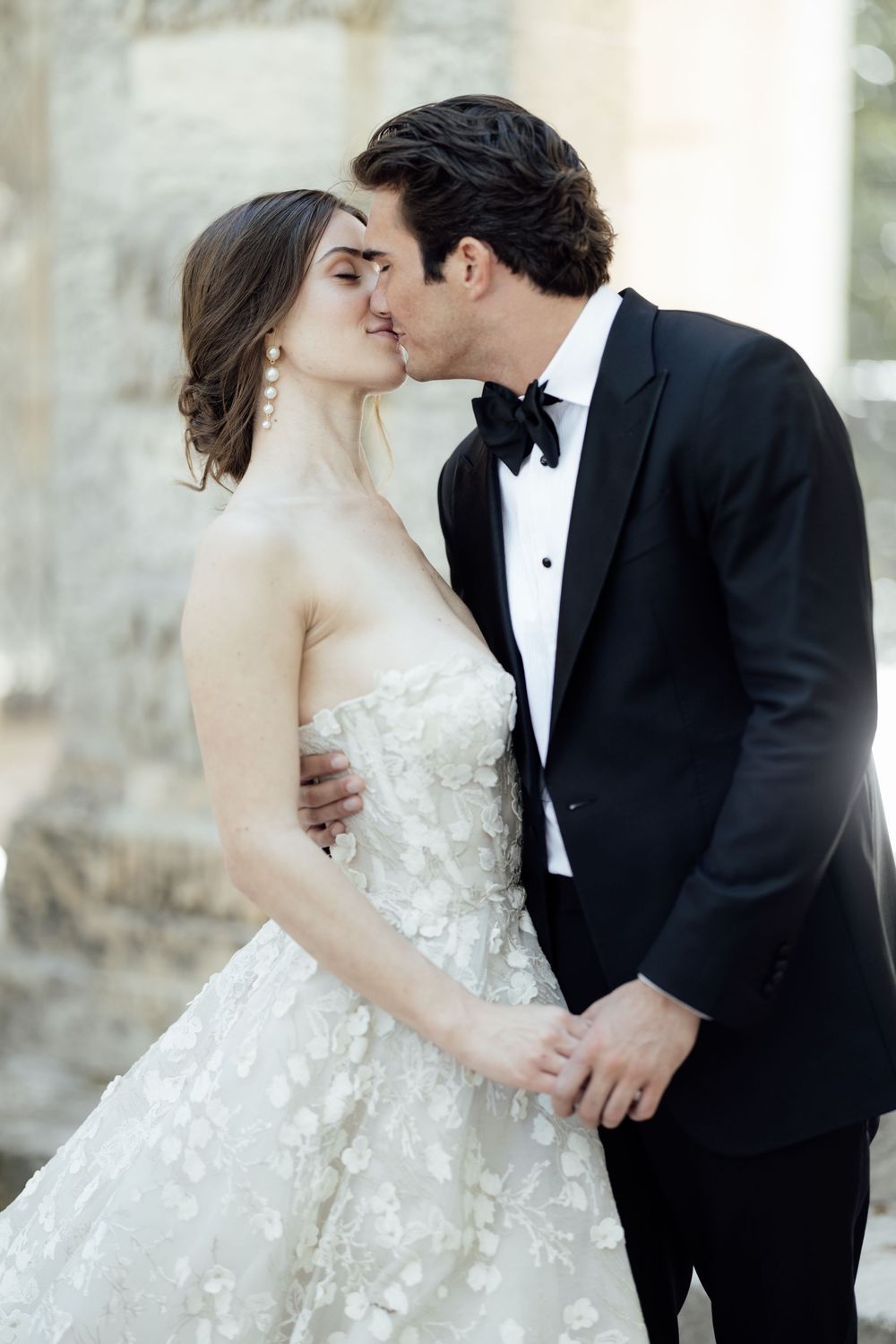 Romantic wedding portrait of couple embracing beneath elegant stone pillars.
