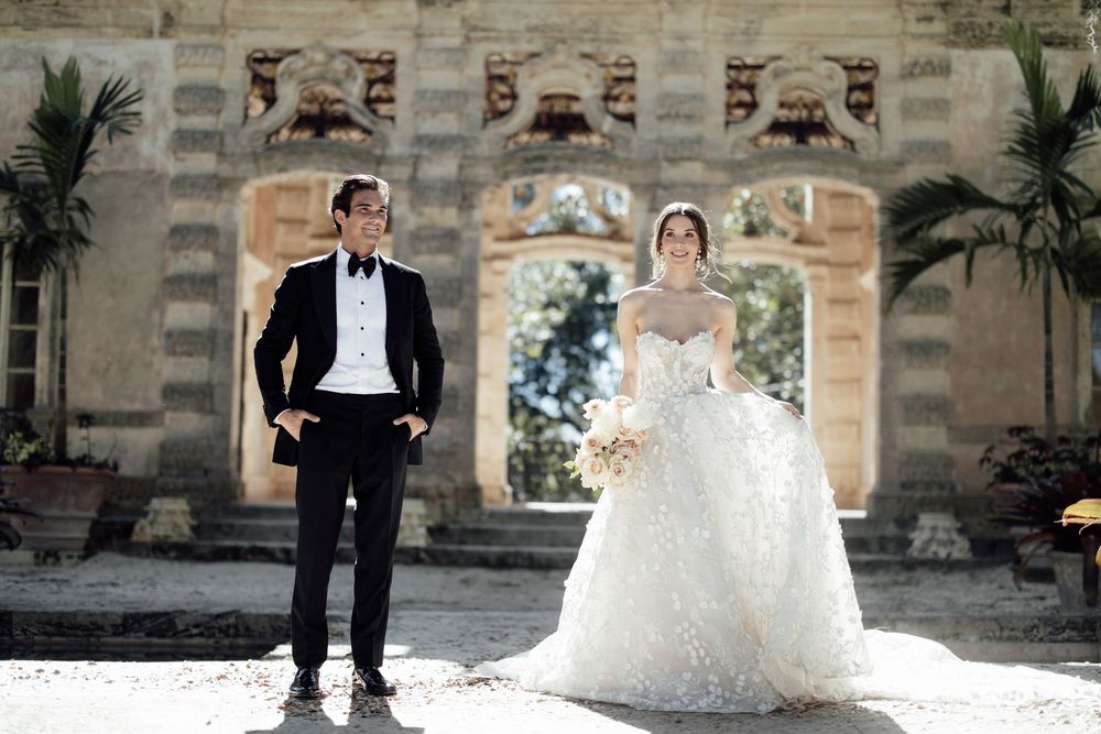 A wedding couple poses for artistic photo sequence against a stone wall backdrop with palm trees.