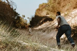 People walking on a narrow hiking trail along a steep mountain ridge at sunset.