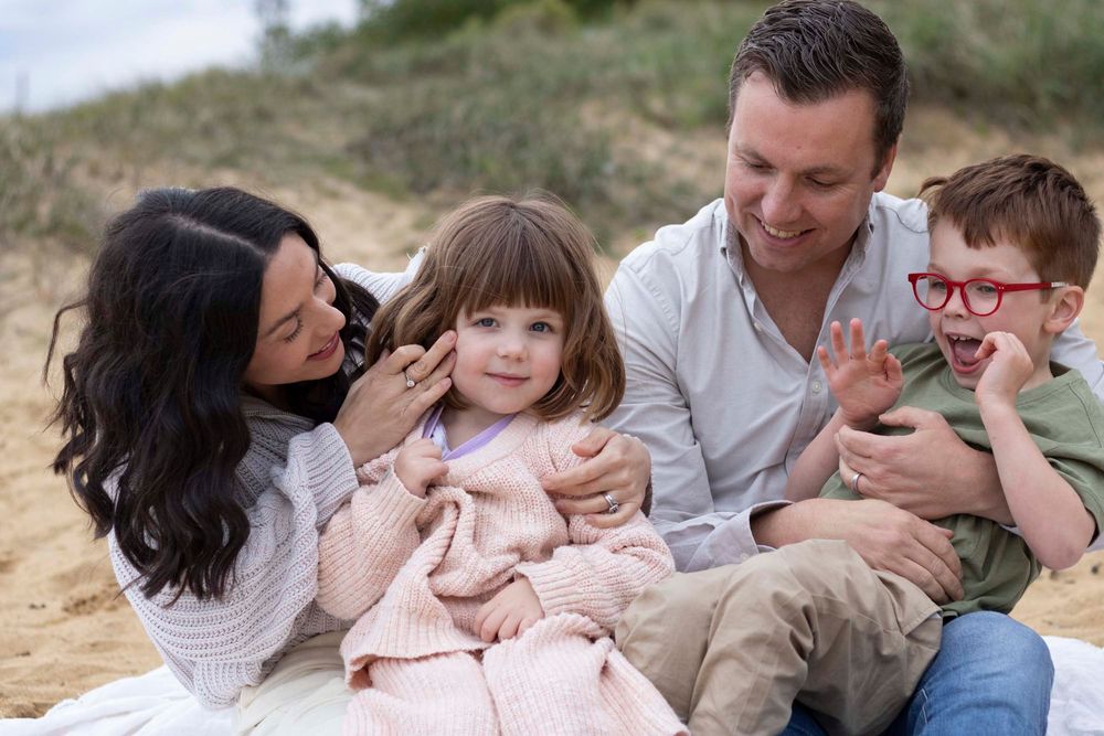 Family members in casual attire sitting and laughing together during a warm outdoor photoshoot on sandy terrain.