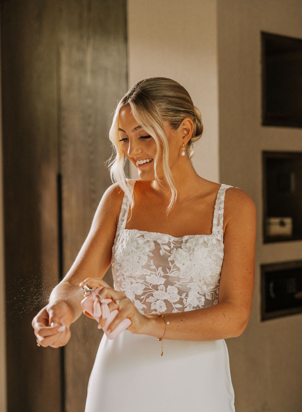 Bride adjusts her fitted white wedding gown with delicate lace details in natural window light.