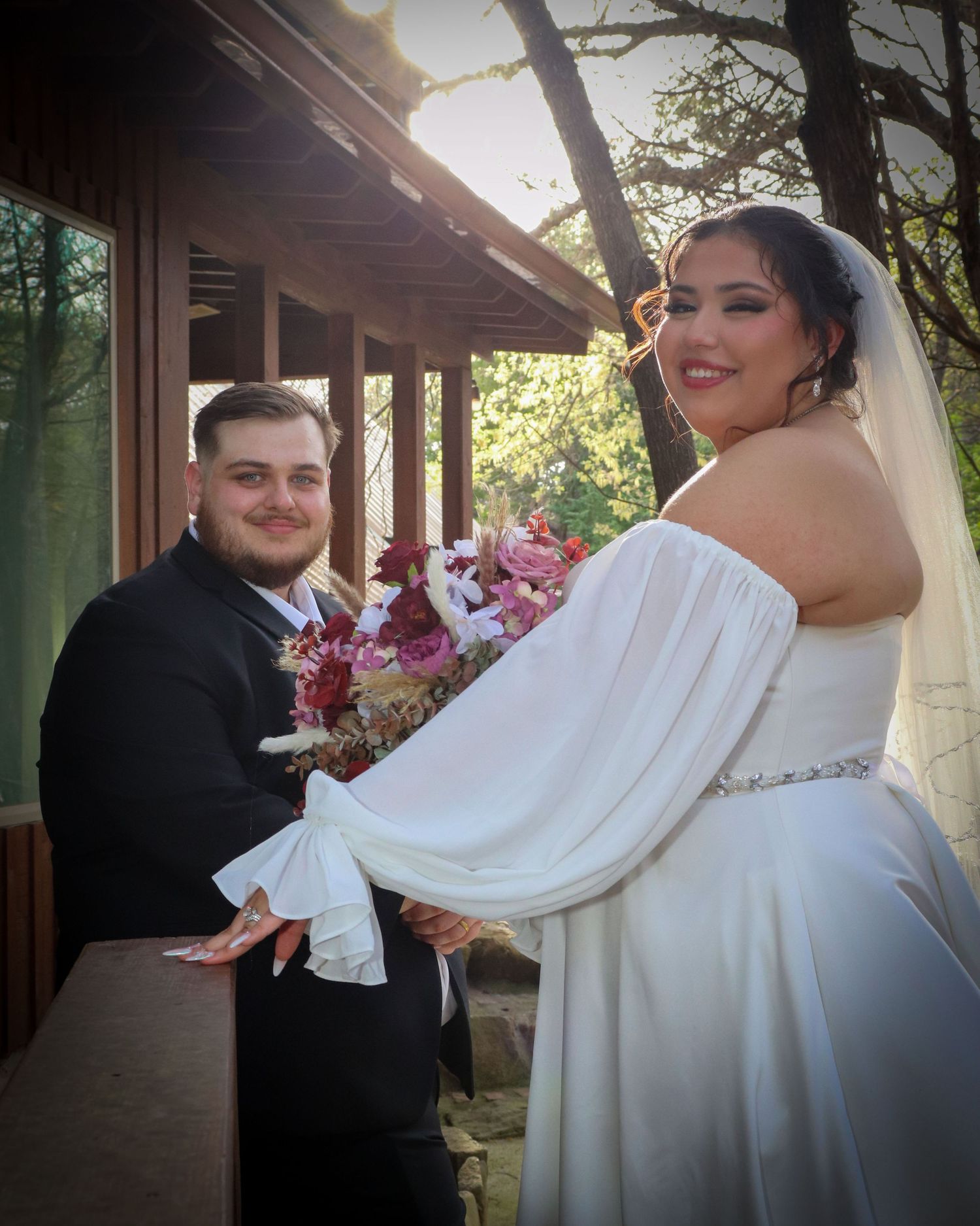 A couple shares a romantic moment in a covered walkway during their wedding photoshoot, displaying their festive attire.