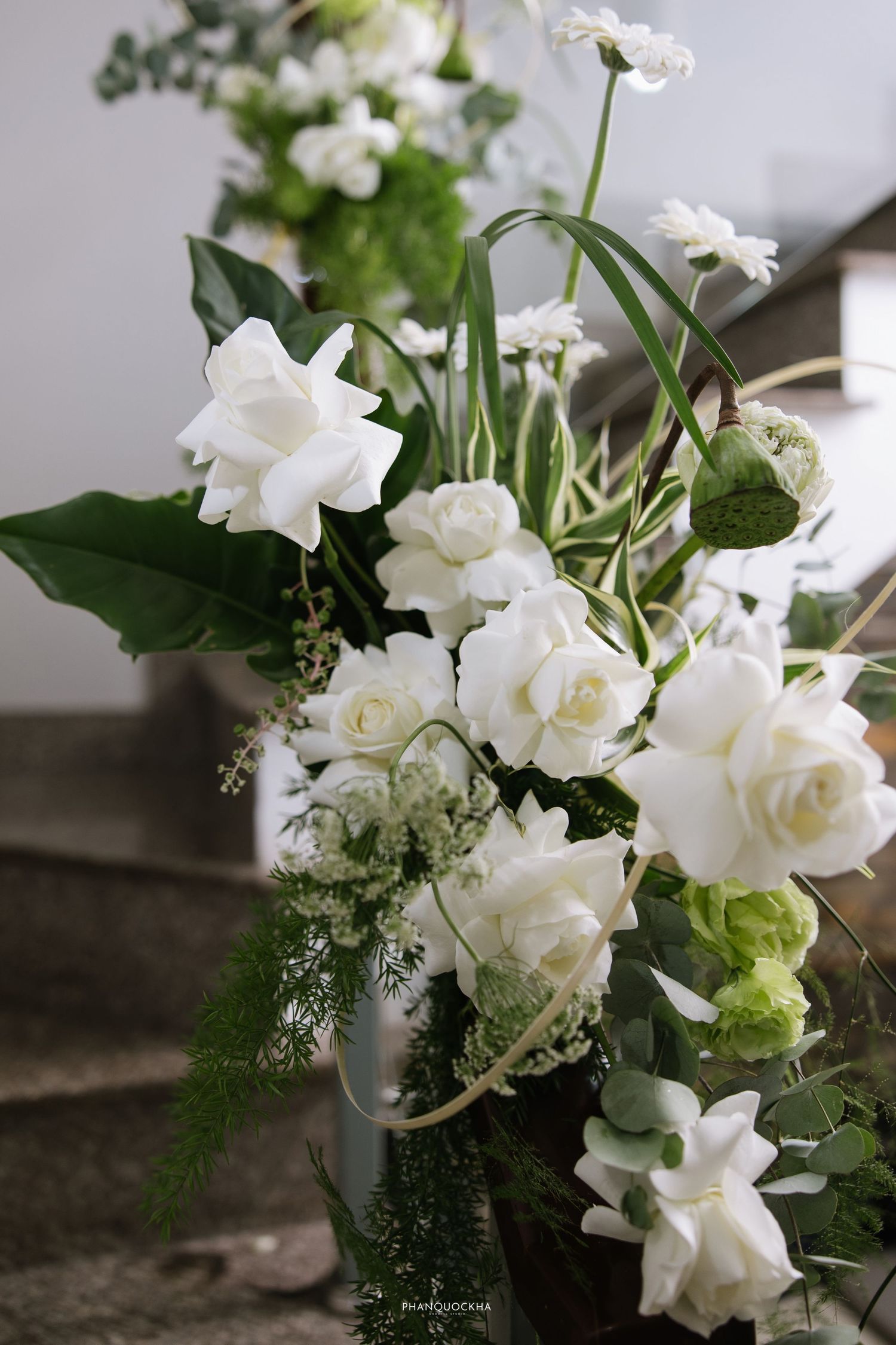 Lush wedding floral arrangement featuring white roses, gardenias, and green foliage displayed on stone steps.