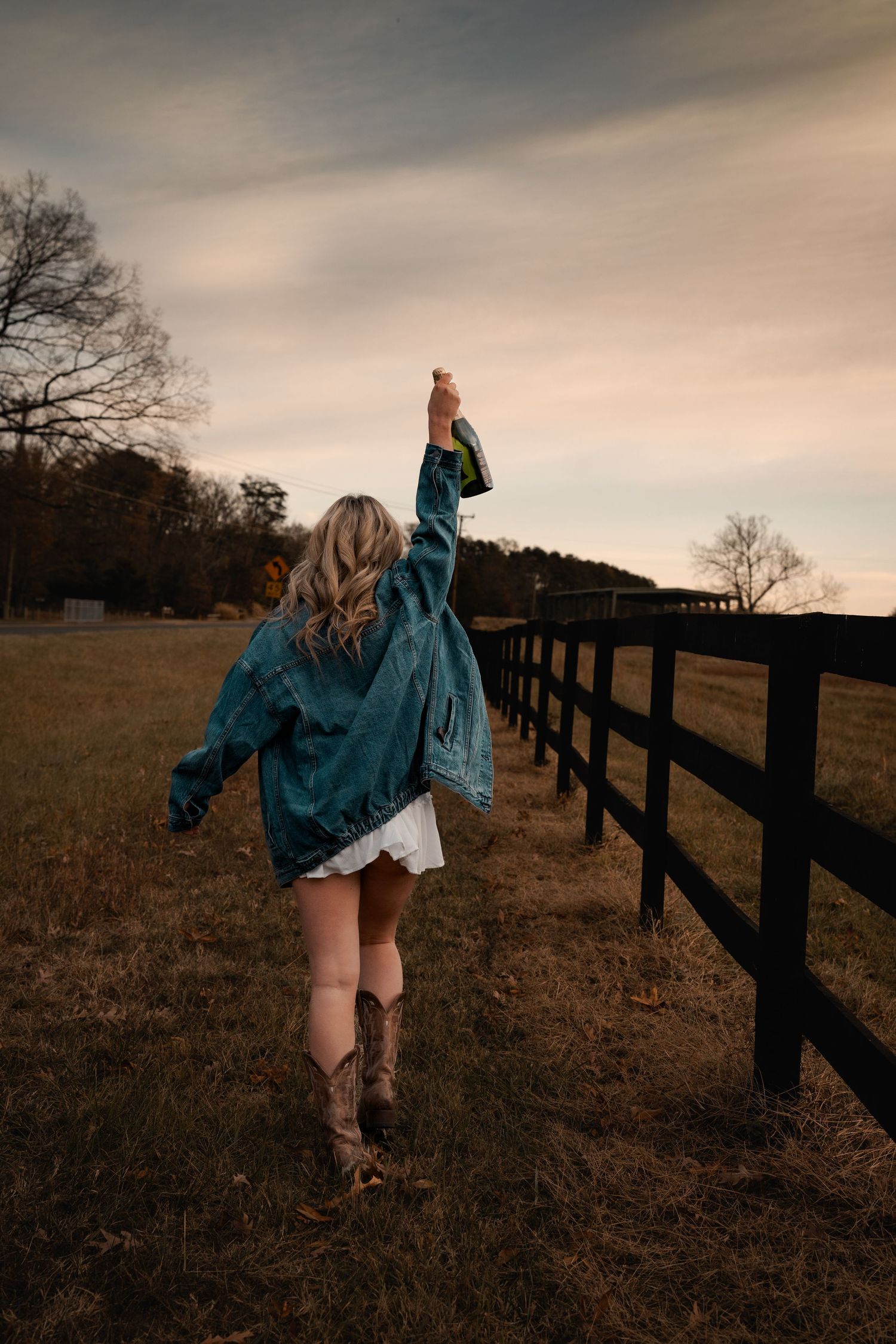 Graduate in teal dress running along wooden fence at Mason Neck, VA during golden hour | Virginia graduation portraits.