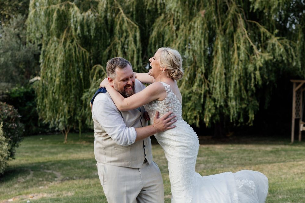 A joyous newlywed couple shares their first dance outdoors beneath a weeping willow tree.