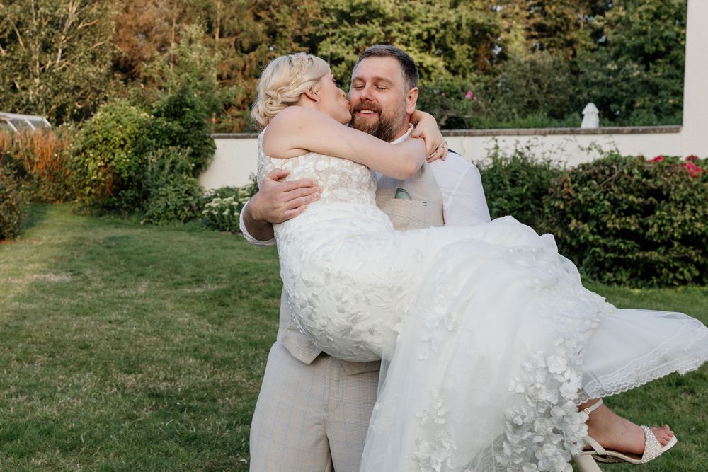 A couple embraces during their outdoor garden wedding ceremony with a traditional dip pose in formal attire.