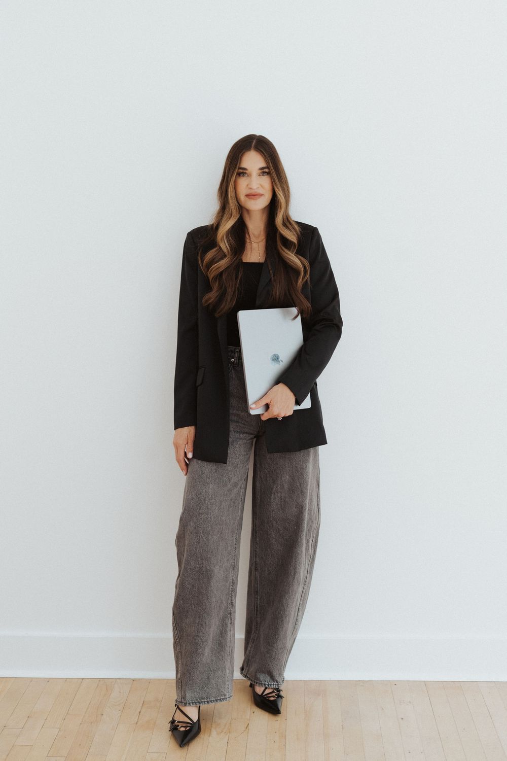 Business casual outfit featuring black blazer and gray pants against white wall.