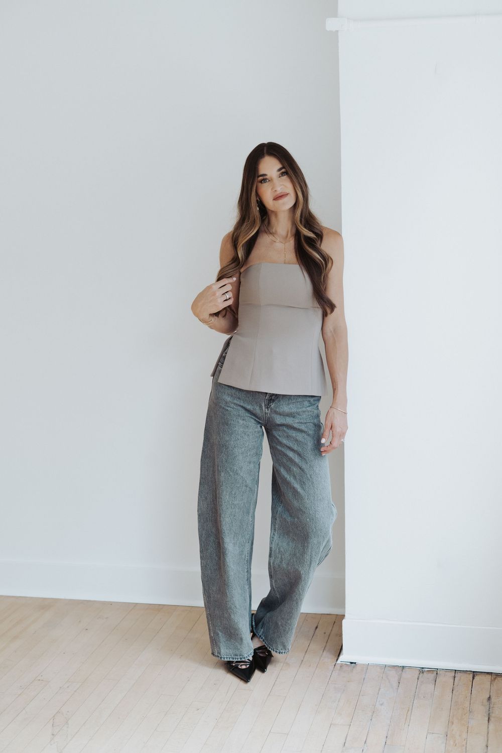 Branding client poses in gray tank top and wide-leg pants against white backdrop.