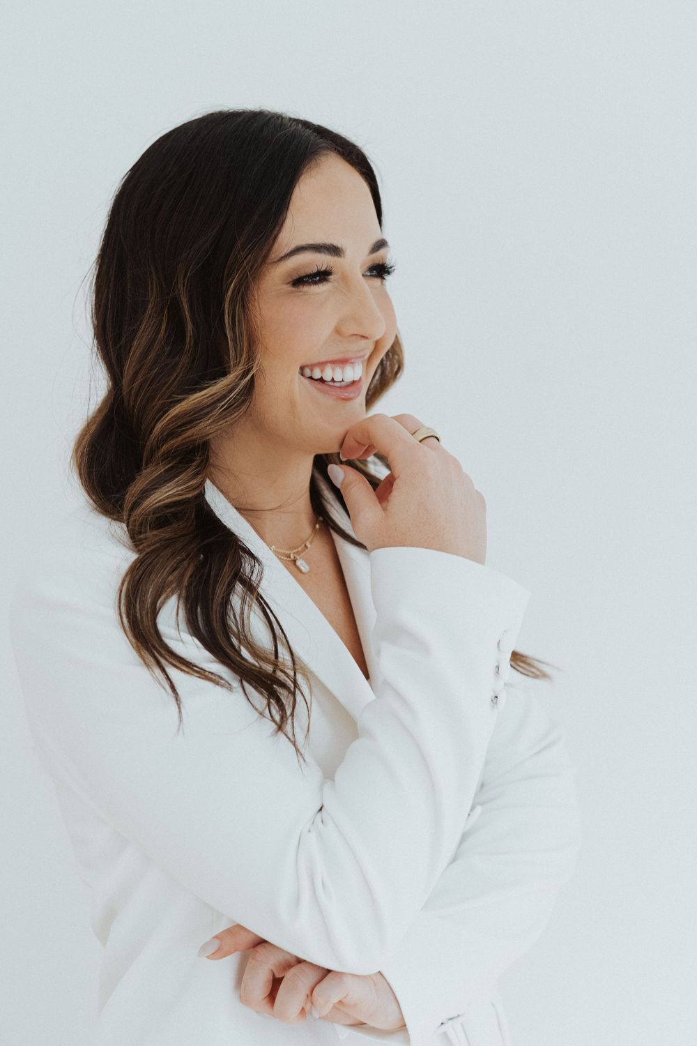 Person in white blazer laughing and posing against white background.