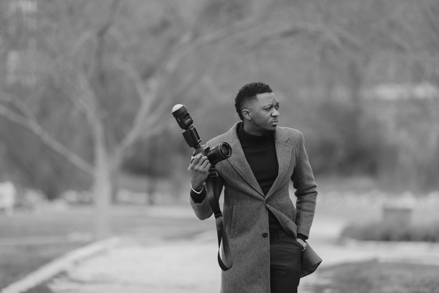A stylish black and white portrait of someone posing with a guitar case outdoors.