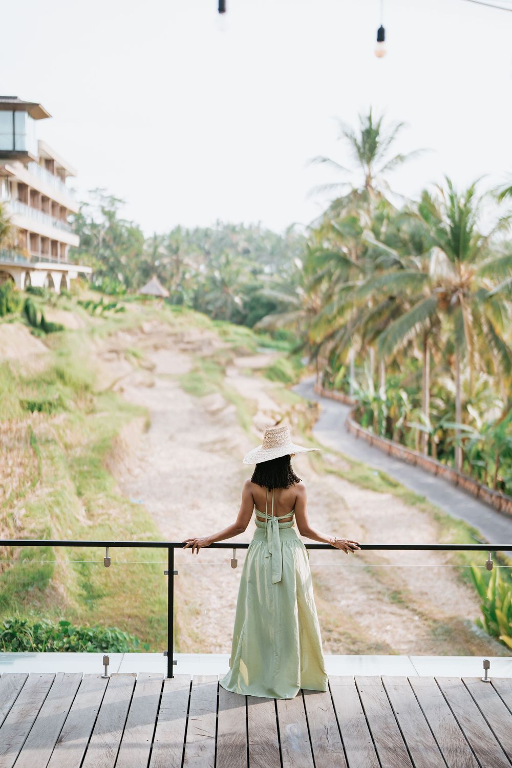 Person in mint dress standing on wooden deck overlooking palm tree landscape.
