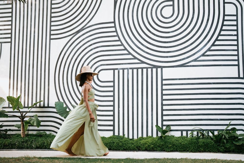 Elegant figure in flowing dress poses against geometric black and white wall pattern with curved lines.