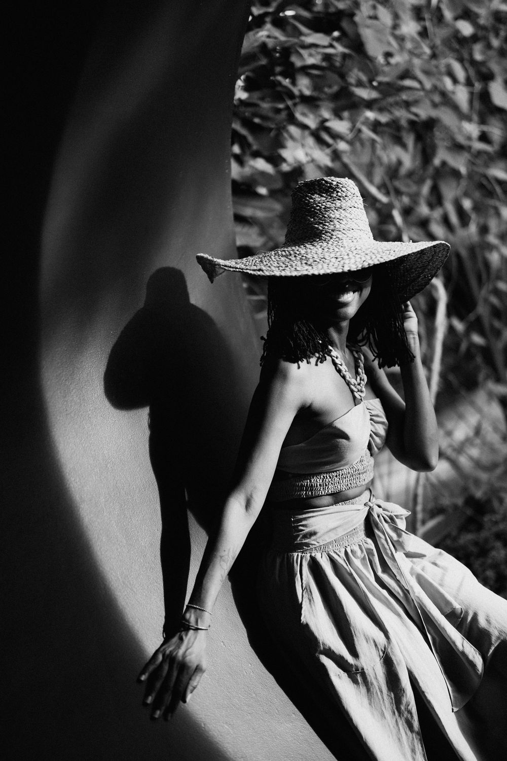Dramatic black and white photo of person in sundress and wide-brimmed hat casting shadow on wall.