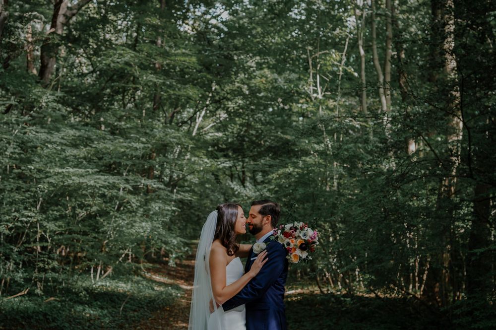 A romantic couple embraces and kisses during their outdoor forest wedding photo session in a lush green setting.