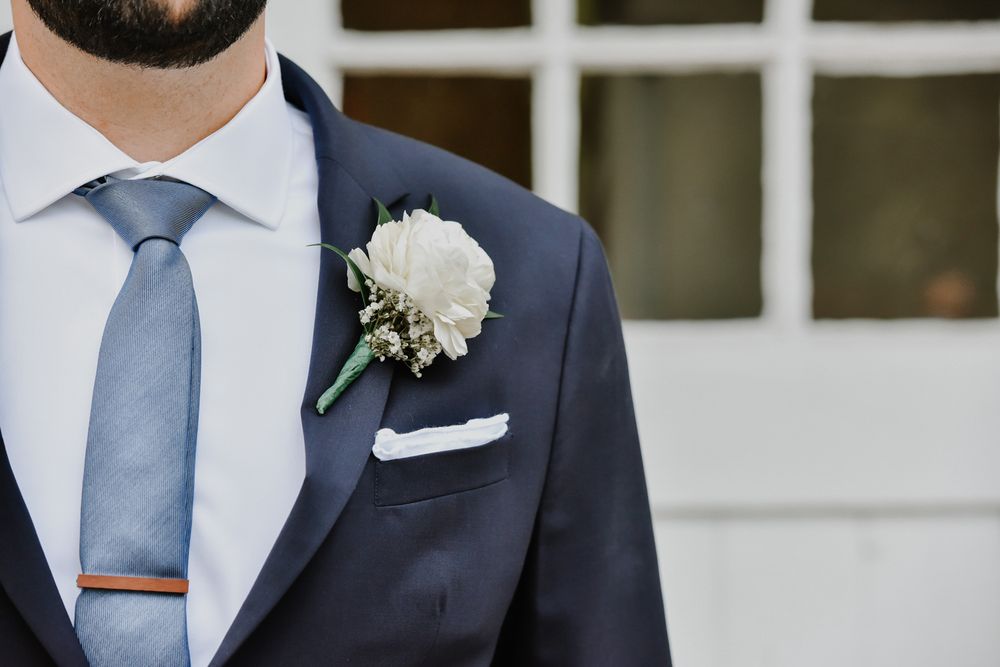 Groom in navy suit with floral boutonniere poses during elegant outdoor wedding ceremony.
