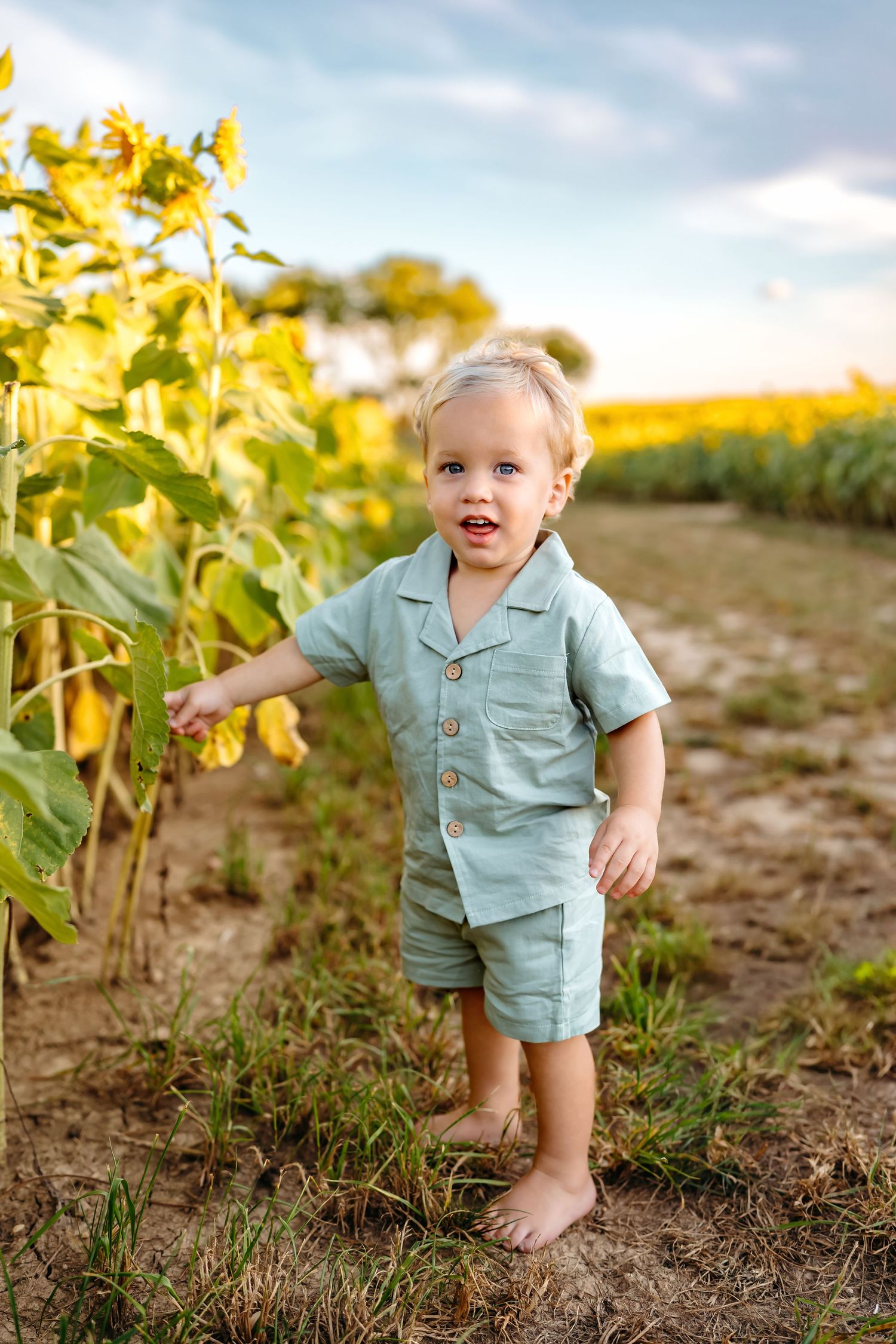 Toddler wearing mint green romper exploring through sunflower field.