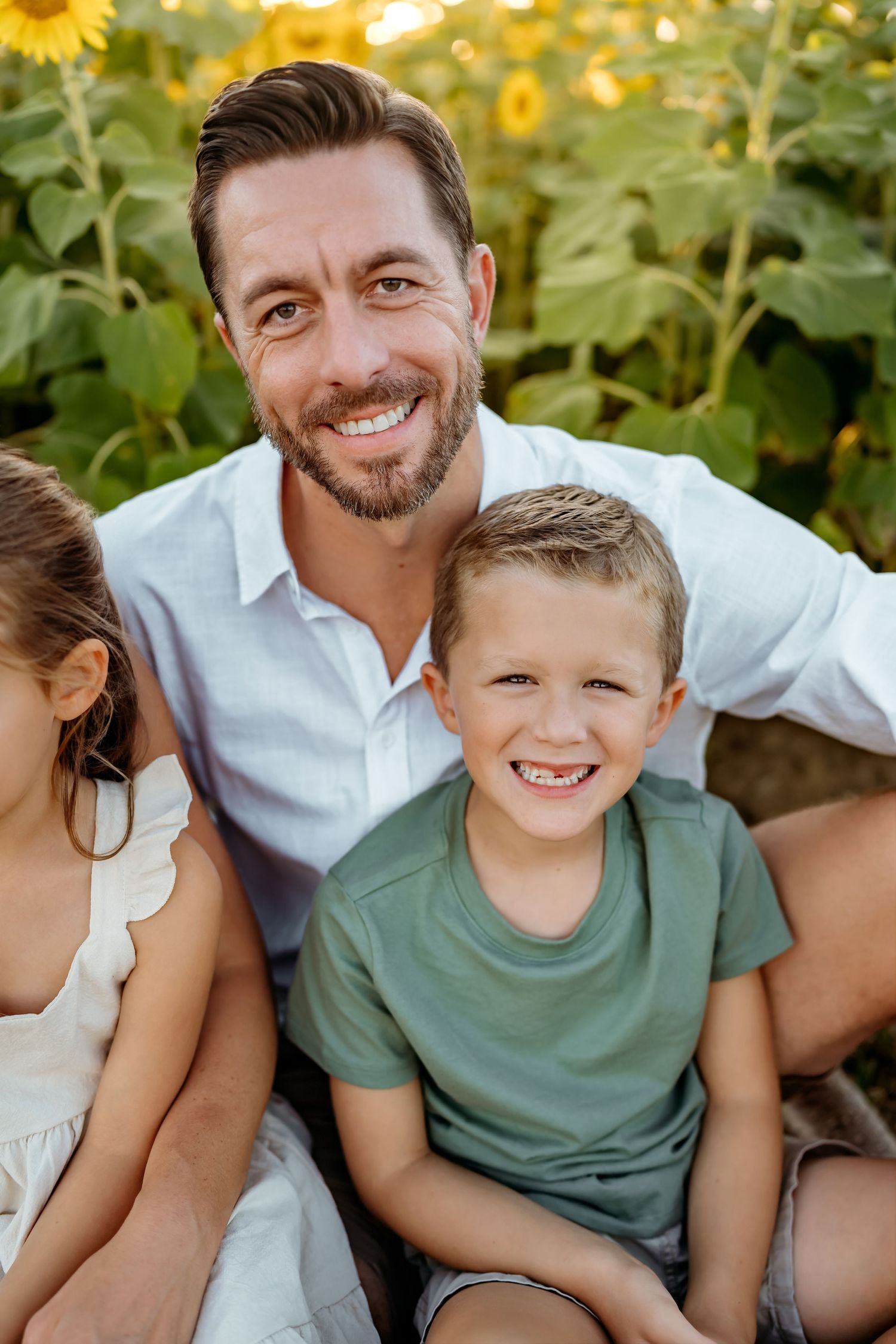 Family enjoying a playful moment together in a sunflower field at sunset.