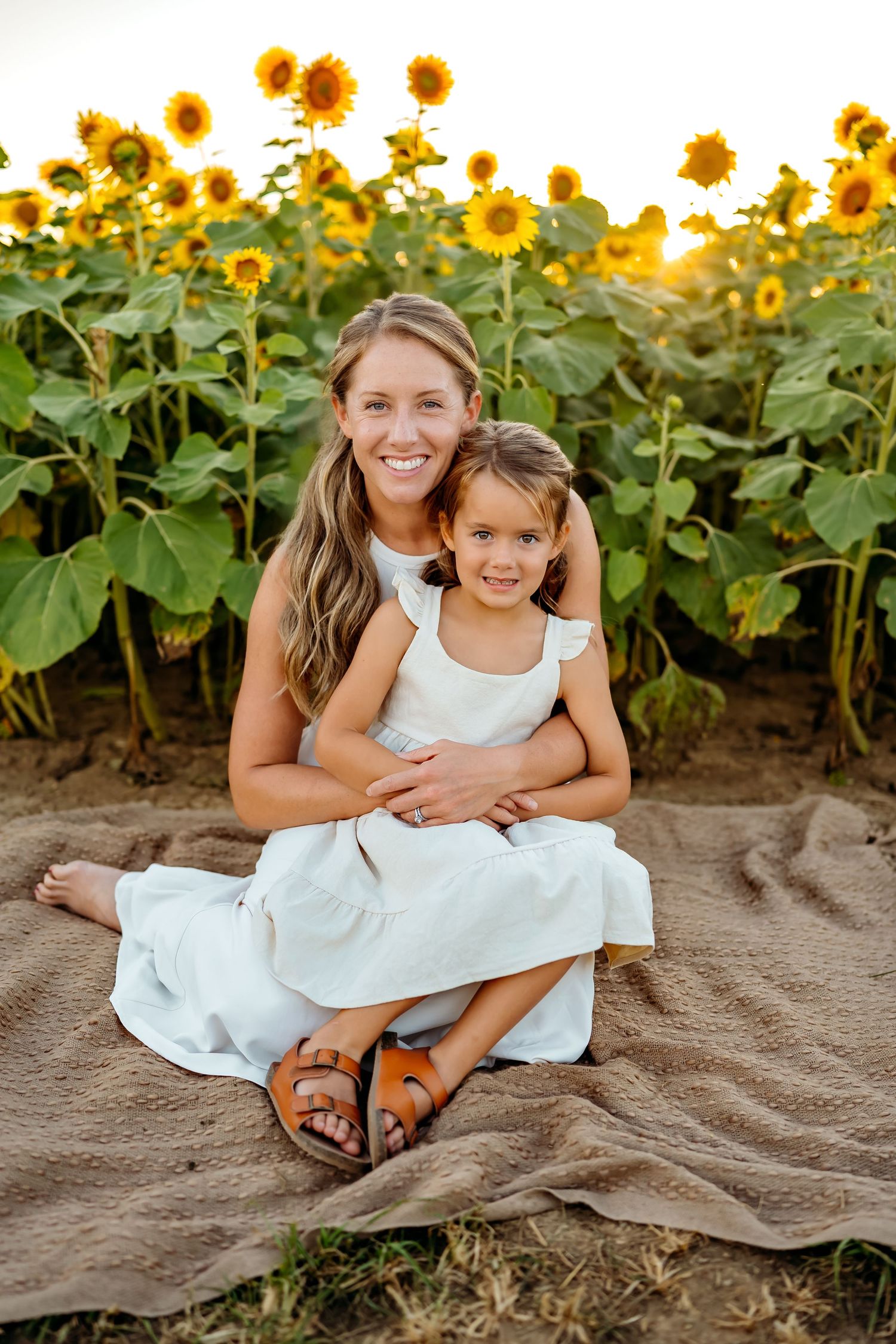 Family portrait in a vibrant sunflower field with white dresses and warm evening light.
