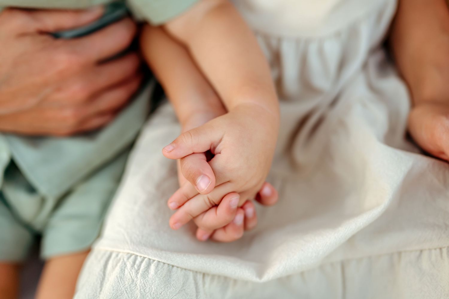Tiny newborn baby hand grasping adult finger while wrapped in soft white blanket.