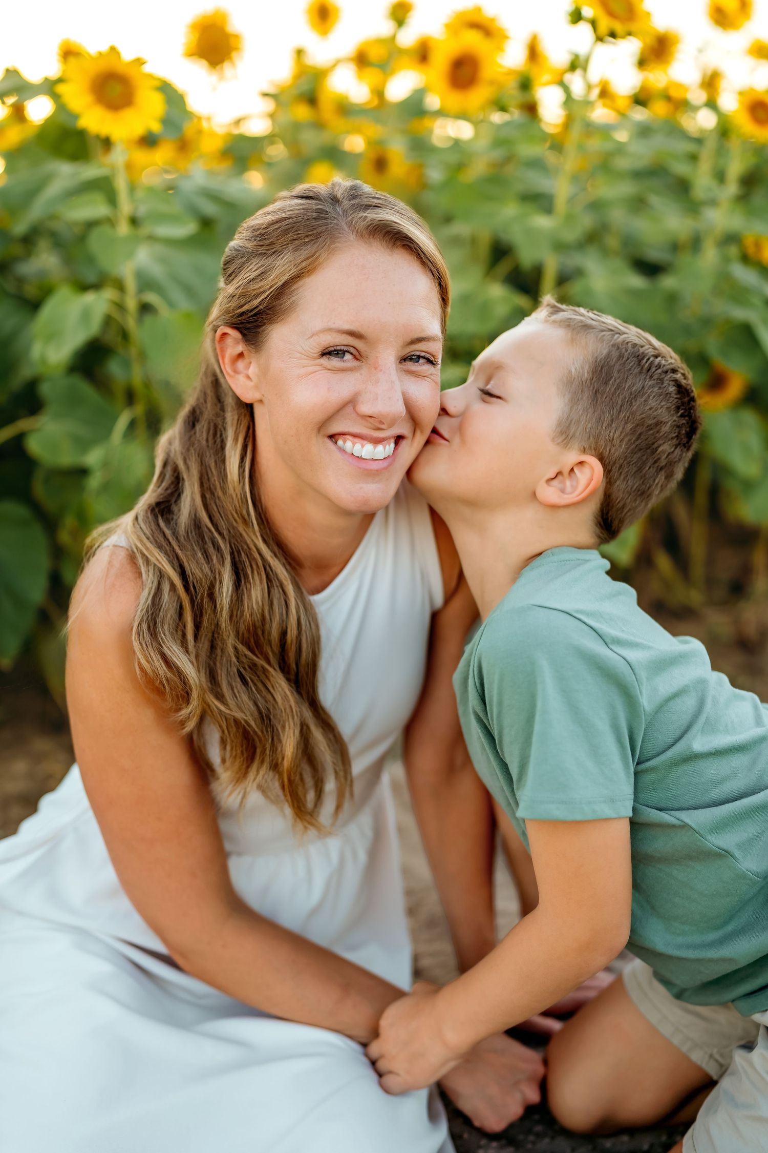 A joyful moment captured in a sunflower field with warm sunlight and natural expressions of affection.