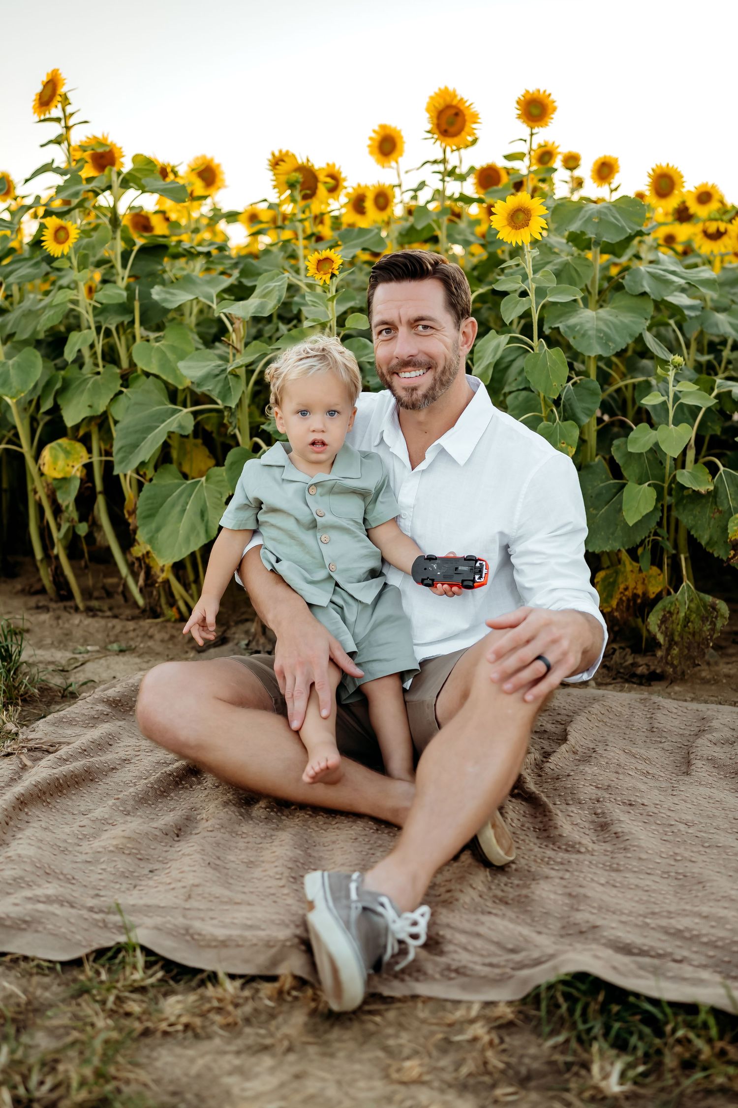 A playful outdoor family photoshoot set against a backdrop of vibrant blooming sunflowers on a sunny day.