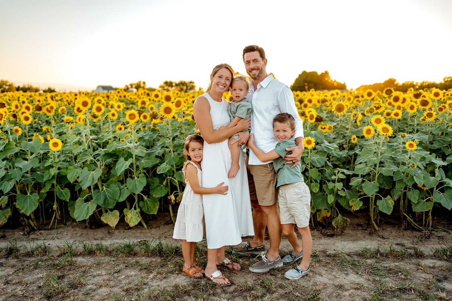 Family enjoying a summer evening photoshoot in a sunflower field at sunset.