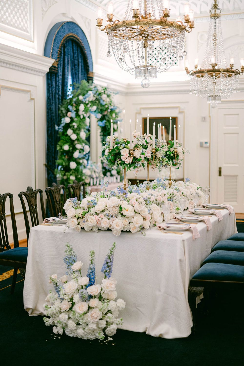 Luxurious white wedding reception tables adorned with cascading floral arrangements under crystal chandeliers.