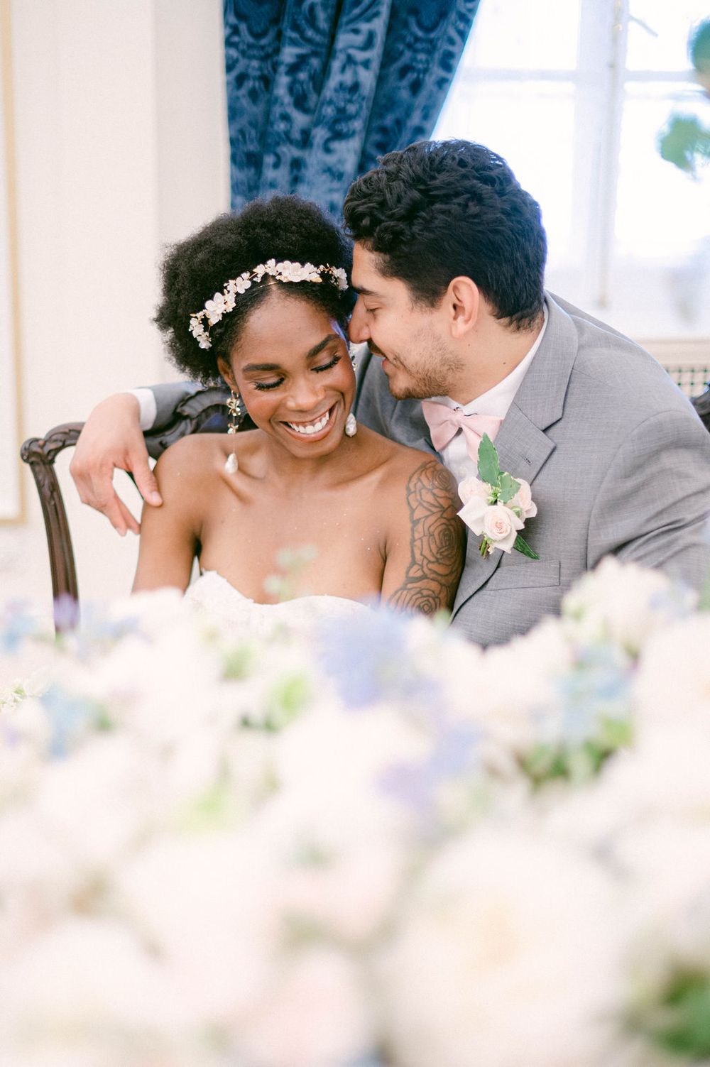 A happy newlywed couple shares an intimate moment at their wedding reception surrounded by soft pastel floral arrangements.